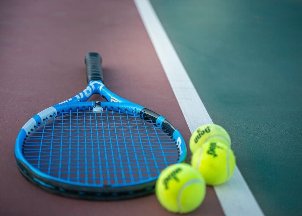 tennis racket on tennis court next to tennis balls